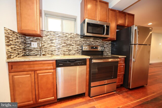 kitchen with light stone counters, wood-type flooring, stainless steel appliances, backsplash, and sink