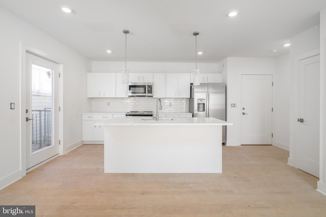 kitchen with pendant lighting, white cabinets, stainless steel appliances, and a center island with sink