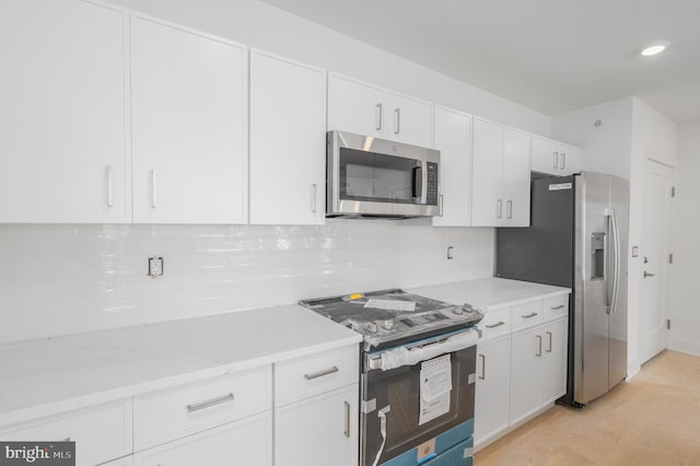 kitchen featuring white cabinets, appliances with stainless steel finishes, decorative backsplash, and light stone counters