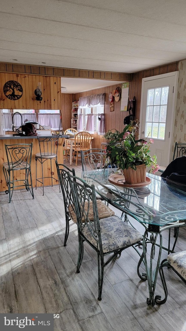 dining space with vaulted ceiling, a textured ceiling, wood walls, and light wood-type flooring