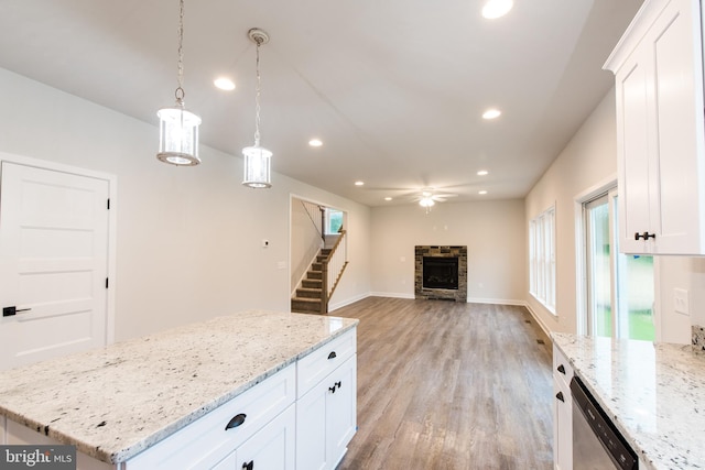 kitchen featuring decorative light fixtures, light stone counters, light hardwood / wood-style floors, a stone fireplace, and white cabinets