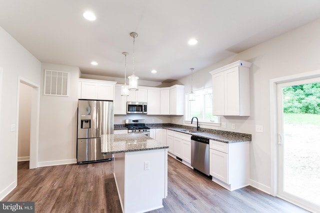 kitchen with appliances with stainless steel finishes, hanging light fixtures, hardwood / wood-style floors, and sink