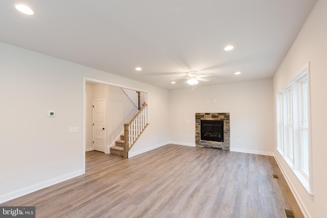 unfurnished living room featuring ceiling fan, light wood-type flooring, and a stone fireplace