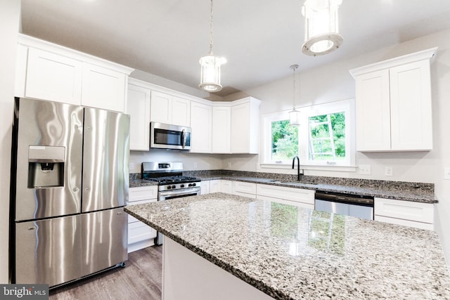 kitchen with appliances with stainless steel finishes, light hardwood / wood-style floors, white cabinets, sink, and hanging light fixtures