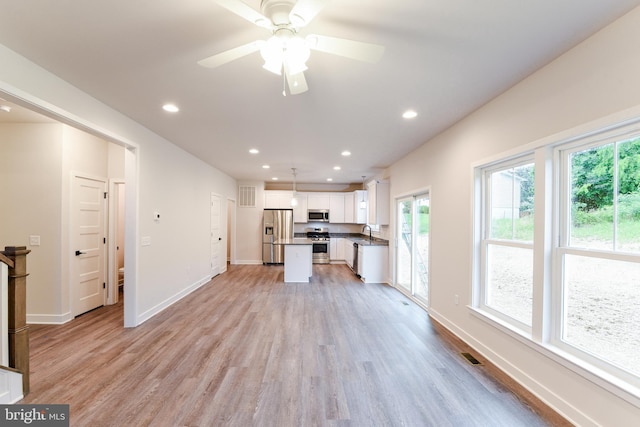 interior space featuring hanging light fixtures, appliances with stainless steel finishes, light hardwood / wood-style floors, white cabinets, and a kitchen island