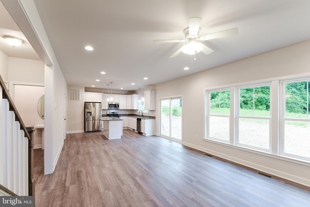 kitchen with appliances with stainless steel finishes, hanging light fixtures, a kitchen island, light hardwood / wood-style floors, and white cabinetry