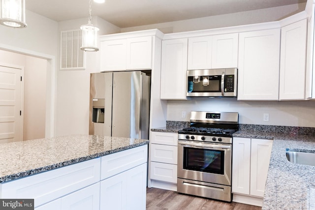 kitchen with white cabinets, appliances with stainless steel finishes, light stone countertops, and light wood-type flooring