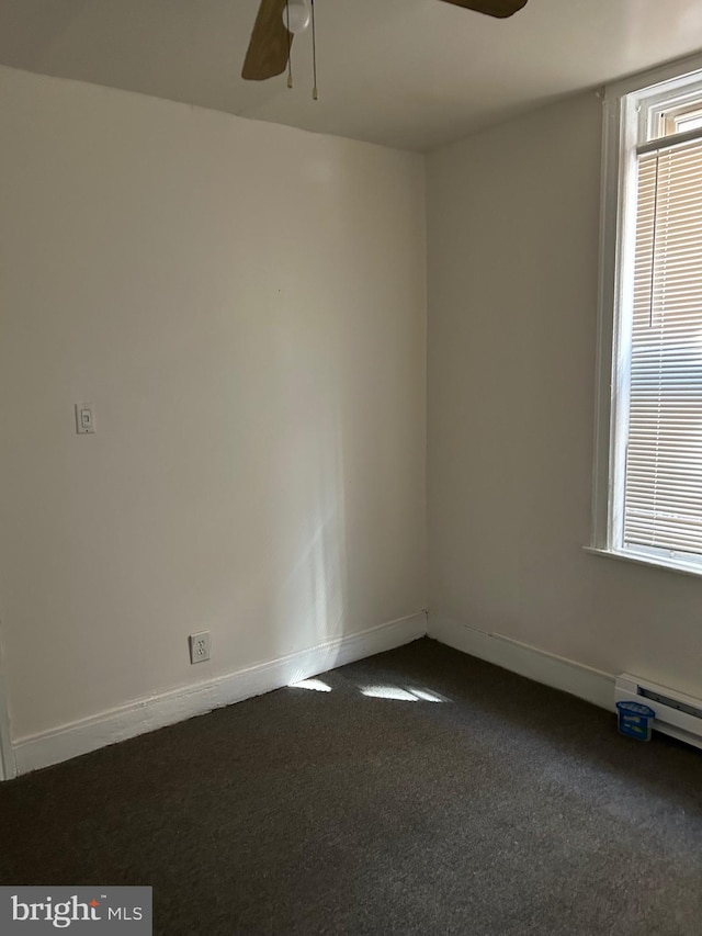 spare room with a baseboard heating unit, dark carpet, and ceiling fan