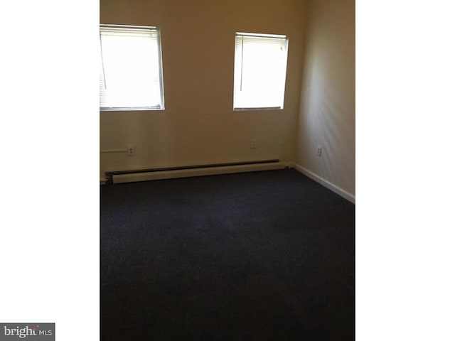 empty room featuring dark carpet, plenty of natural light, and a baseboard heating unit