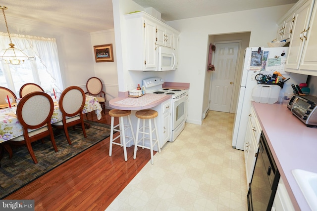 kitchen with decorative light fixtures, a breakfast bar, white cabinets, white appliances, and light hardwood / wood-style floors