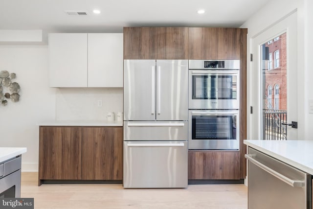 kitchen with light hardwood / wood-style floors, appliances with stainless steel finishes, white cabinetry, and decorative backsplash