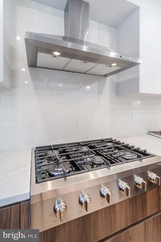 kitchen with white cabinets, stainless steel gas stovetop, ventilation hood, and backsplash