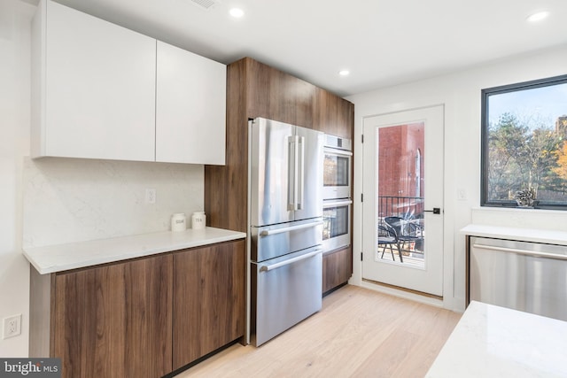 kitchen featuring light hardwood / wood-style flooring, a wealth of natural light, stainless steel appliances, and white cabinets