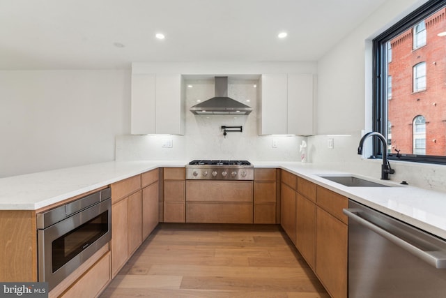 kitchen with wall chimney range hood, white cabinets, stainless steel appliances, light hardwood / wood-style floors, and sink