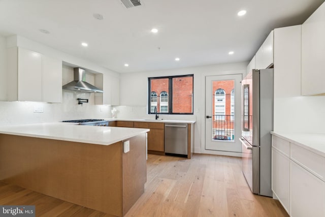 kitchen featuring white cabinetry, wall chimney range hood, stainless steel appliances, and light wood-type flooring