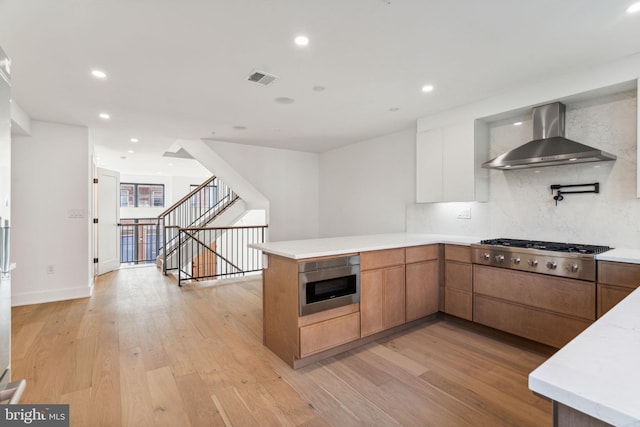 kitchen featuring stainless steel gas cooktop, wall chimney range hood, backsplash, light hardwood / wood-style floors, and built in microwave