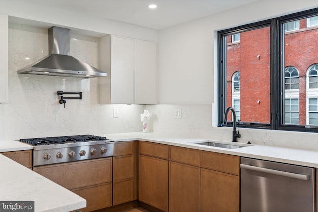 kitchen with stainless steel appliances, backsplash, sink, and wall chimney range hood