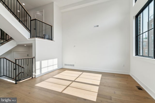 unfurnished living room with light hardwood / wood-style floors and a towering ceiling