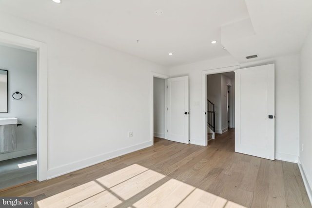 unfurnished bedroom with connected bathroom and light wood-type flooring