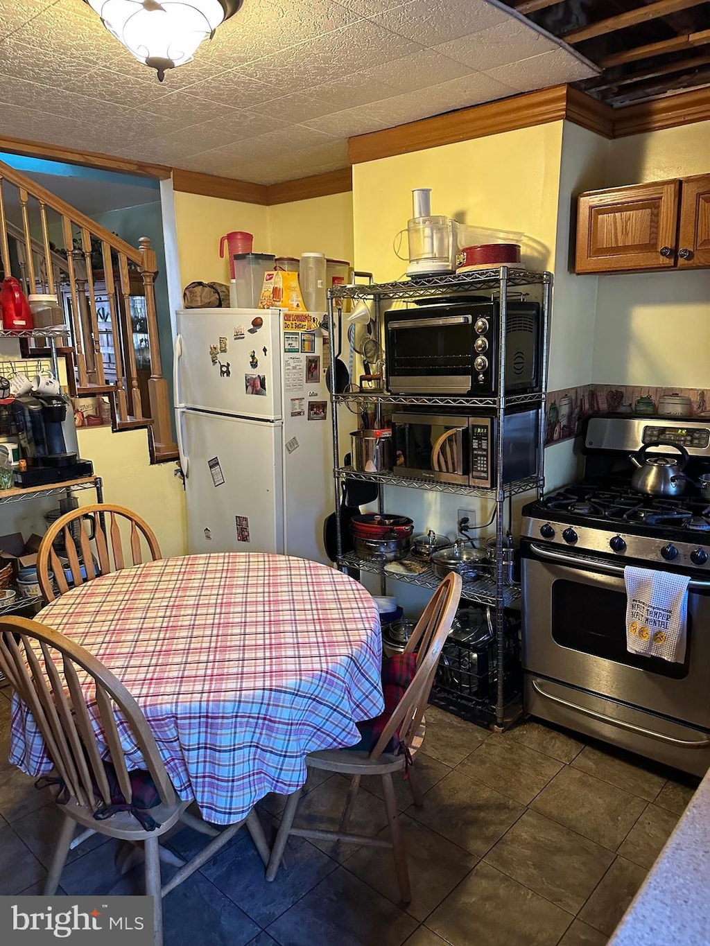 kitchen featuring dark tile floors, white fridge, gas stove, and crown molding