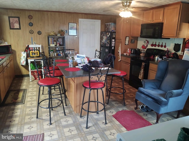 kitchen with a breakfast bar area, a center island, wooden walls, black appliances, and ceiling fan