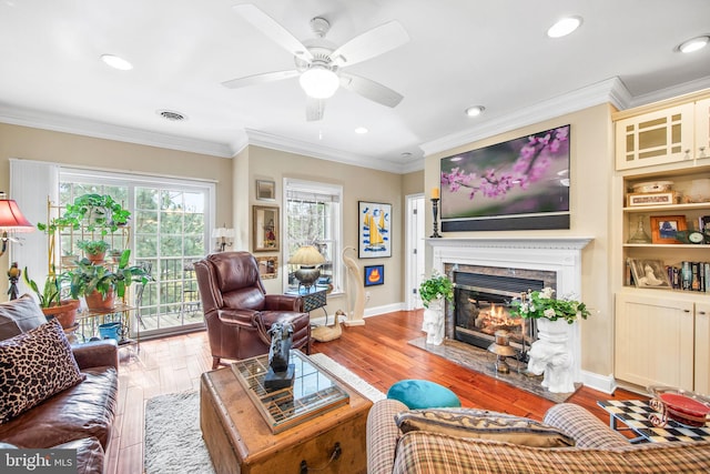 living room featuring hardwood / wood-style floors, a fireplace, ceiling fan, and crown molding