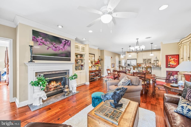 living room with hardwood / wood-style floors, a high end fireplace, ornamental molding, and ceiling fan with notable chandelier