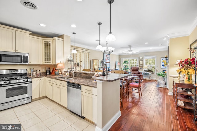 kitchen with pendant lighting, kitchen peninsula, stainless steel appliances, and cream cabinets