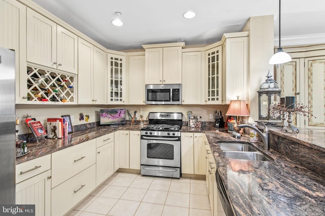 kitchen with dark stone counters, appliances with stainless steel finishes, decorative light fixtures, sink, and cream cabinetry