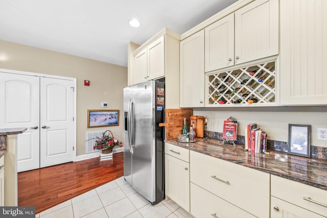 kitchen featuring dark stone counters, stainless steel fridge with ice dispenser, light hardwood / wood-style flooring, and cream cabinetry