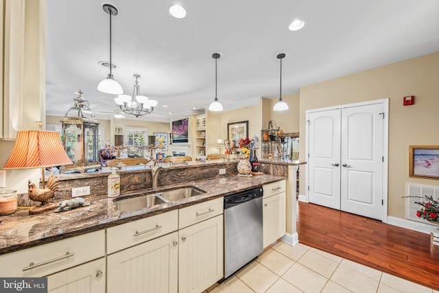 kitchen featuring dark stone counters, hanging light fixtures, light hardwood / wood-style floors, dishwasher, and cream cabinetry