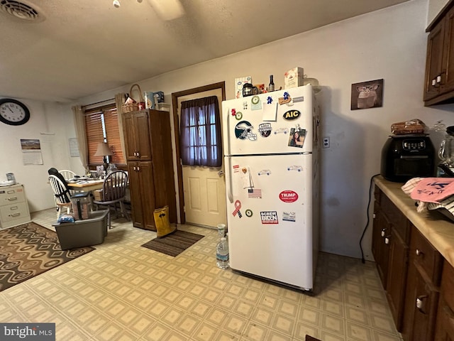 kitchen with light tile floors, dark brown cabinets, and white fridge