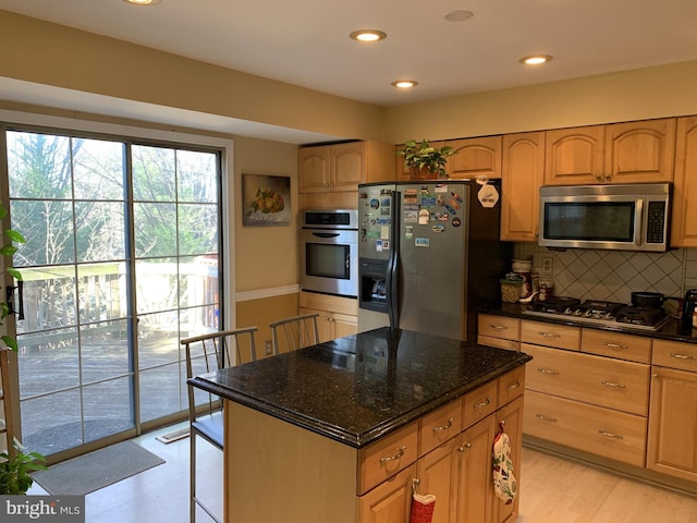 kitchen featuring light hardwood / wood-style flooring, stainless steel appliances, dark stone countertops, a center island, and tasteful backsplash