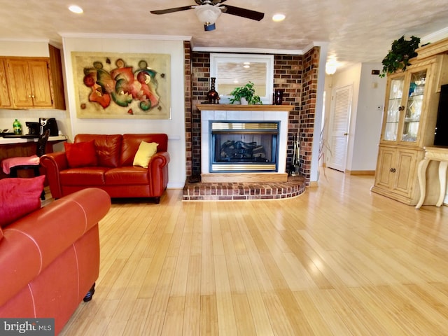 living room with ceiling fan, ornamental molding, a fireplace, and light wood-type flooring