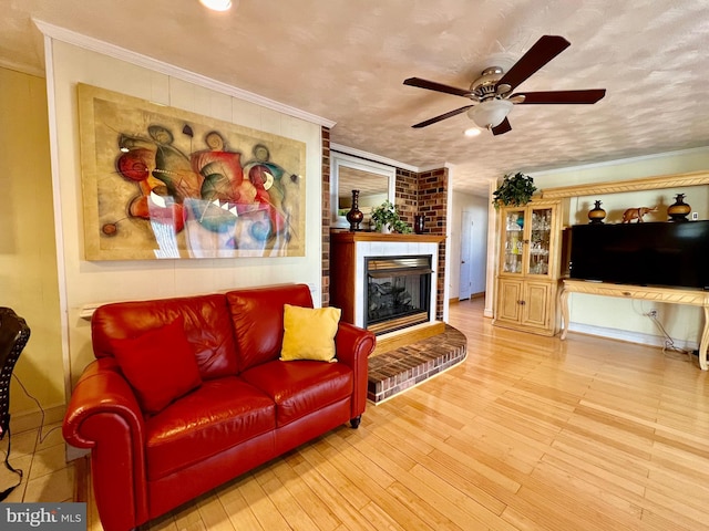 living room featuring light hardwood / wood-style floors, a brick fireplace, brick wall, crown molding, and ceiling fan