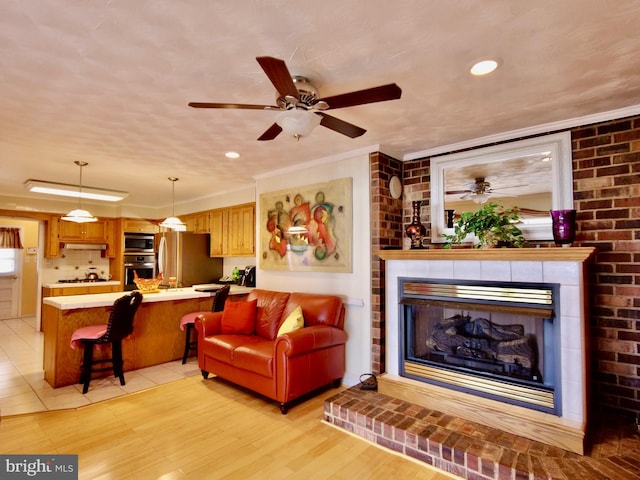 living room featuring ceiling fan, ornamental molding, light hardwood / wood-style flooring, and a fireplace