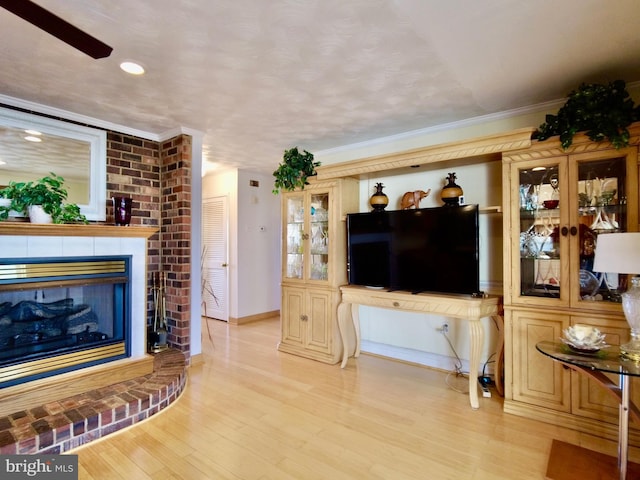 living room with light hardwood / wood-style floors, ornamental molding, a fireplace, and ceiling fan