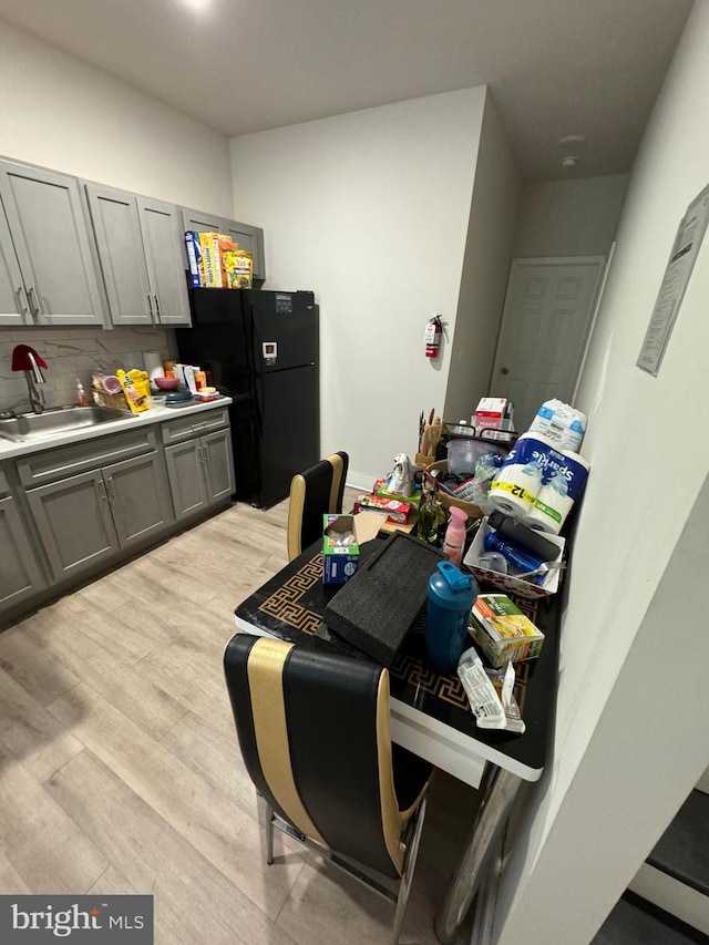 interior space featuring black refrigerator, gray cabinets, sink, tasteful backsplash, and light hardwood / wood-style floors