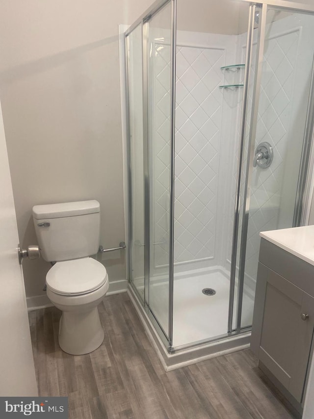 bathroom with hardwood / wood-style flooring, a shower with shower door, toilet, and vanity