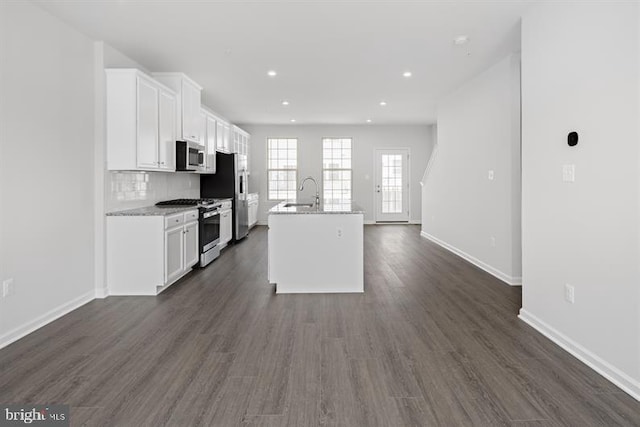 kitchen with dark hardwood / wood-style flooring, appliances with stainless steel finishes, white cabinets, and an island with sink