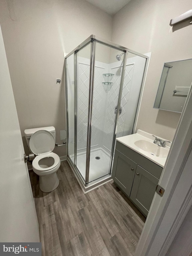 bathroom with walk in shower, hardwood / wood-style floors, vanity, and toilet