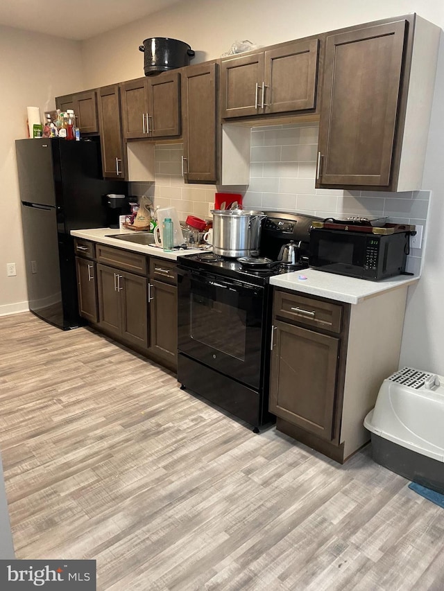 kitchen with dark brown cabinetry, decorative backsplash, black appliances, and light wood-type flooring