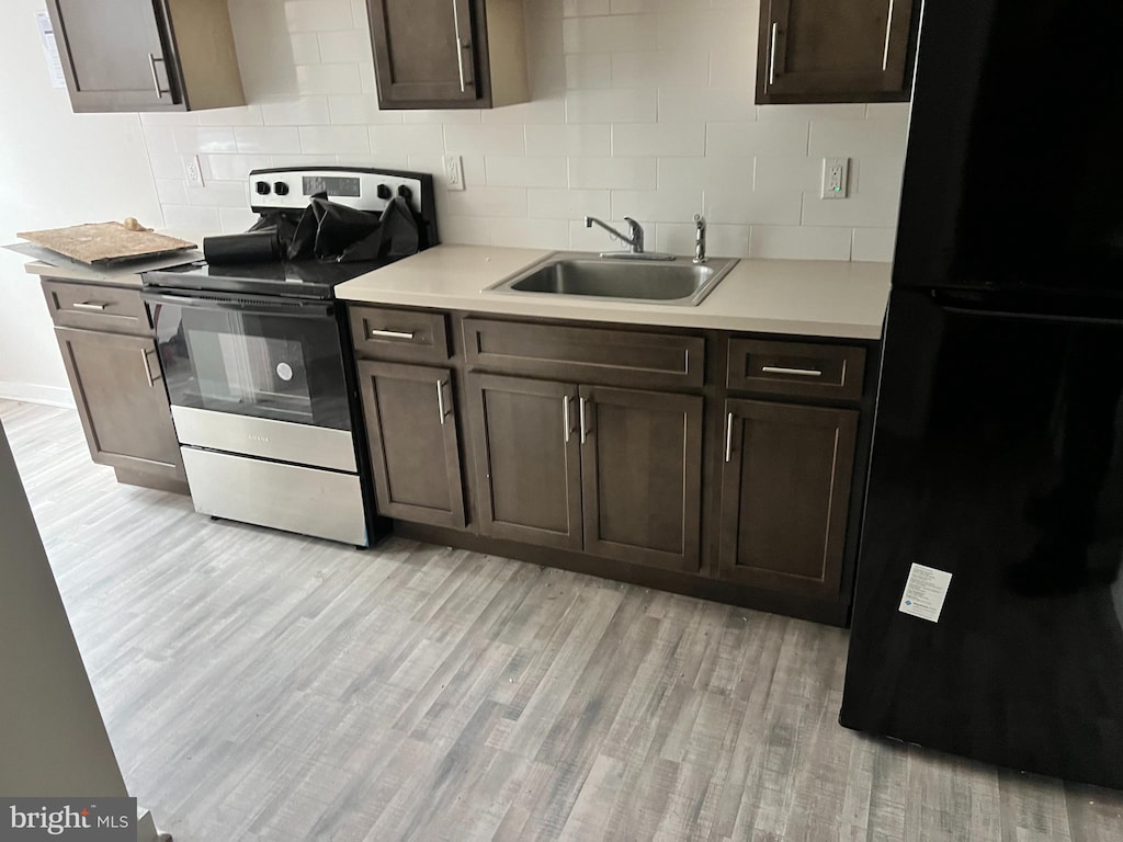 kitchen featuring dark brown cabinets, light hardwood / wood-style flooring, black fridge, electric range, and sink