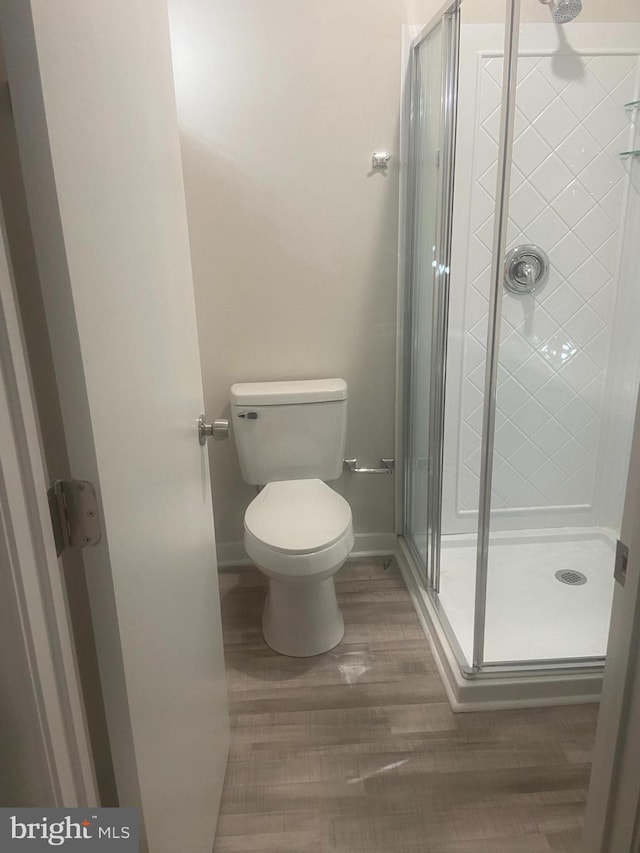 bathroom with hardwood / wood-style floors, an enclosed shower, and toilet