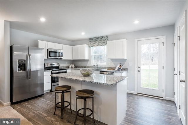 kitchen with dark hardwood / wood-style floors, white cabinetry, appliances with stainless steel finishes, and a kitchen island