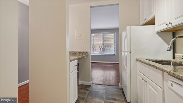 kitchen with light stone counters, white appliances, dark tile flooring, sink, and white cabinets