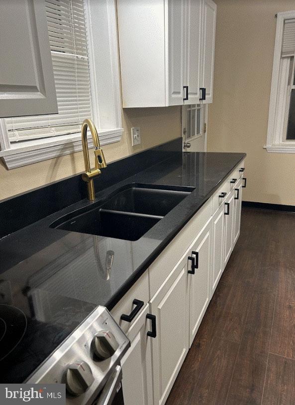 kitchen featuring stove, white cabinetry, dark wood-type flooring, and sink