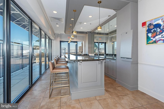 kitchen featuring pendant lighting, dark stone counters, a kitchen breakfast bar, ornamental molding, and a kitchen island with sink