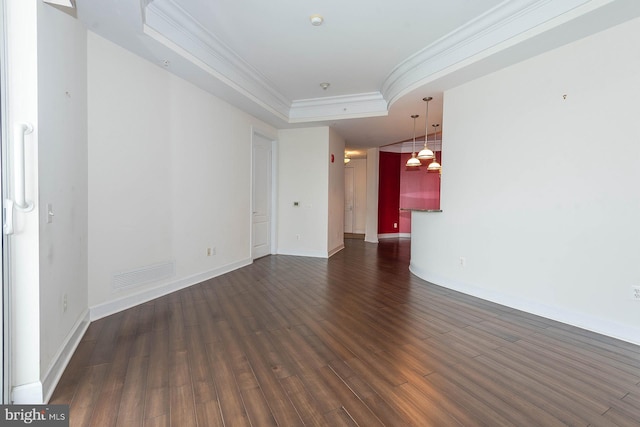 empty room with dark wood-type flooring, a tray ceiling, and ornamental molding