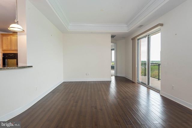 empty room featuring a healthy amount of sunlight, a raised ceiling, and dark wood-type flooring